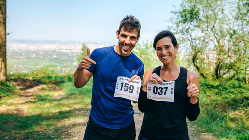 Portrait of happy couple holding marathon bibs while standing on field