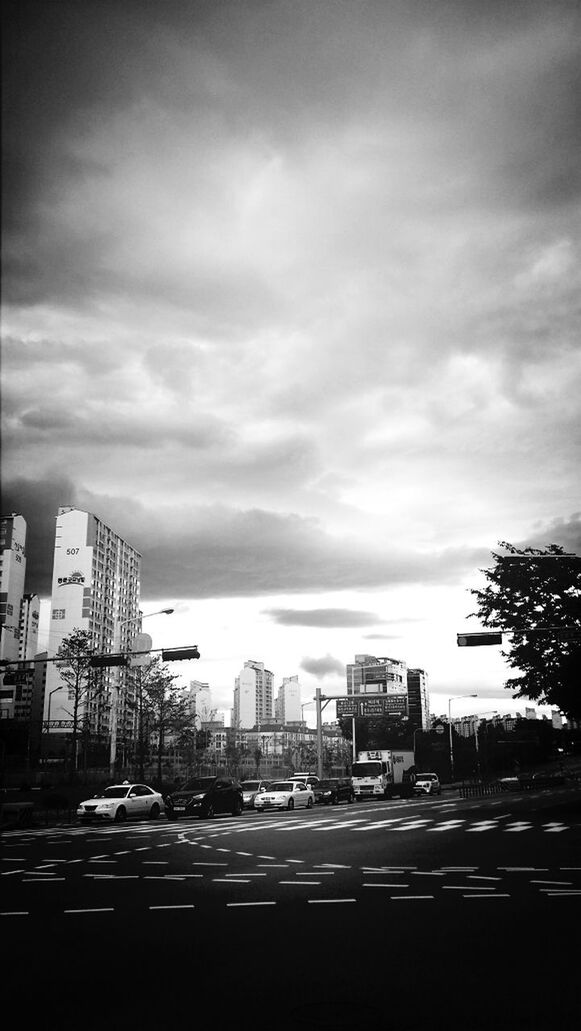 building exterior, architecture, built structure, city, sky, car, transportation, street, road, land vehicle, cloud - sky, cloudy, mode of transport, city life, building, city street, cloud, cityscape, road marking, residential building