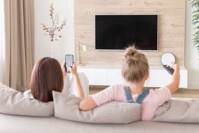 Woman using smart phone sitting by daughter on sofa at home