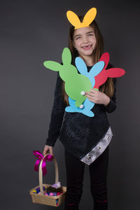 Portrait of smiling girl with eater bunny and pom pom in basket against gray background