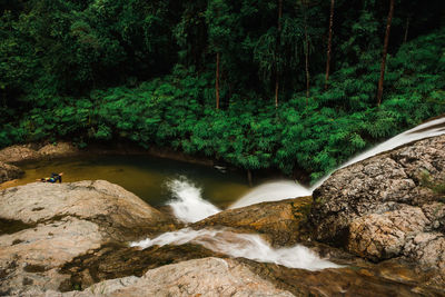 Woman relaxing on rock by waterfall in forest