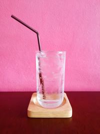 Close-up of water in glass with straw on table against wall