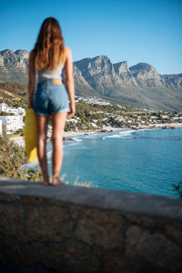 Rear view of woman standing by sea against mountains