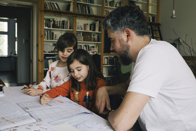 Twin girls doing homework while sitting by father at table