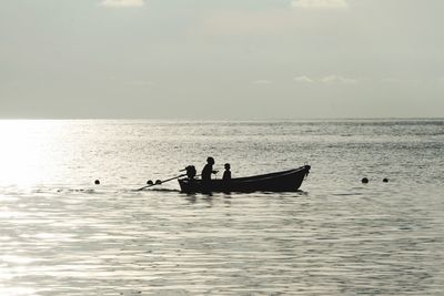 Silhouette people in boat on sea against sky