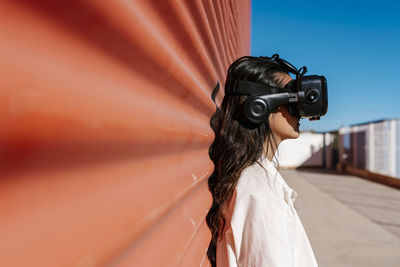 Woman with virtual reality headset leaning on red wall