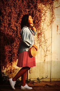 Full length of woman holding smart phone while standing against wall
