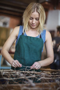 Young blond female worker tying rope while making chaise longue at workshop