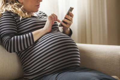 Midsection of man using mobile phone while sitting on sofa