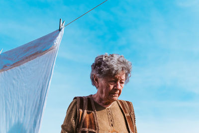 Low angle view of senior woman against blue sky.