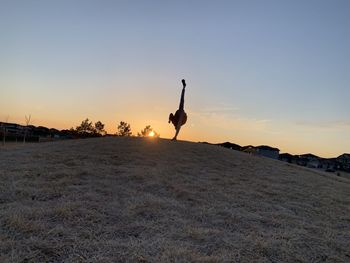 Silhouette man jumping on land against sky during sunset