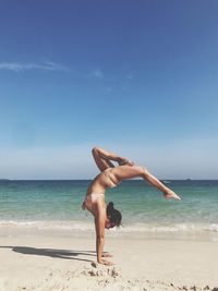 Full length of woman wearing bikini while practicing yoga at beach against sky