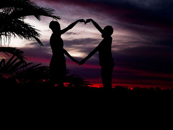 Silhouette people standing on land against sky during sunset