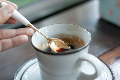 Close-up of hand holding coffee cup on table