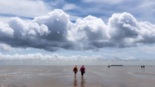 Rear view of people at beach against cloudy sky