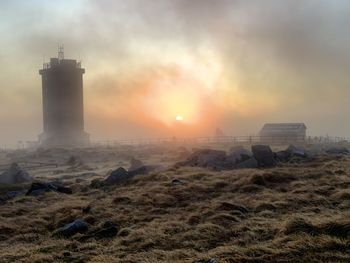 Lighthouse on land by buildings against sky during sunset