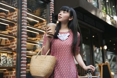 Young woman looking away while standing by store