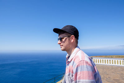 Close-up of young man looking at sea against clear blue sky