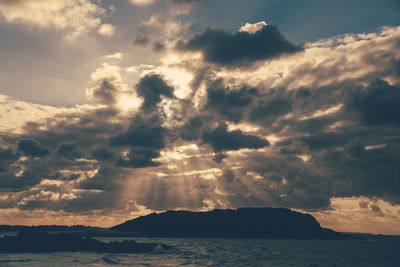 Silhouette mountain in sea against cloudy sky