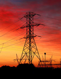Low angle view of silhouette electricity pylon against orange sky