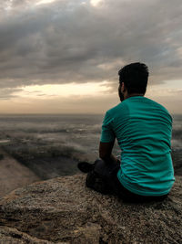 Rear view of man sitting on rock against sky