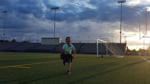 Boy running on sports field against cloudy sky