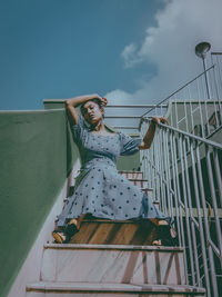 Low angle view of woman sitting on staircase against sky