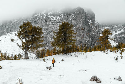 Rear view of female hiker walking on snowy path under amazing misty mountains