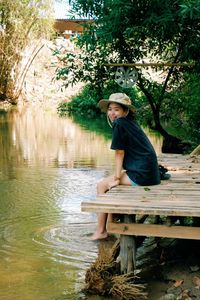 Full length of man sitting by lake against trees