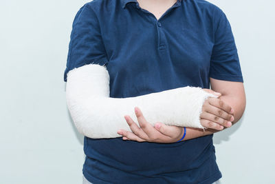 Midsection of boy with fracture hand standing against wall