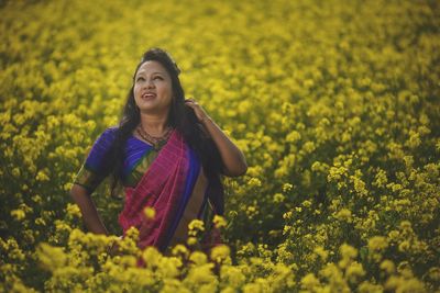 Portrait of woman standing amidst yellow flowering plants on field