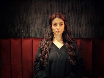 Portrait of young woman standing against curtain