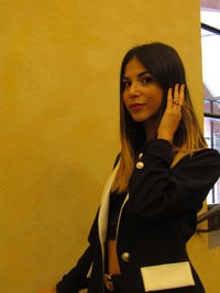 Portrait of smiling young woman standing against yellow wall