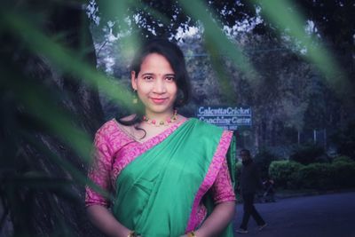 Portrait of smiling young woman standing against trees