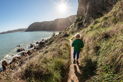 Preschooler walking on seaside mountain path on sunny day in new zealand