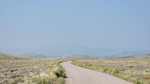 Dirt road along countryside landscape against clear sky