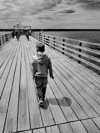 Rear view of boy standing on pier at sea