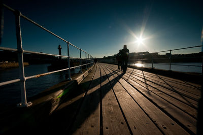 Wooden pier over river against sky during sunny day