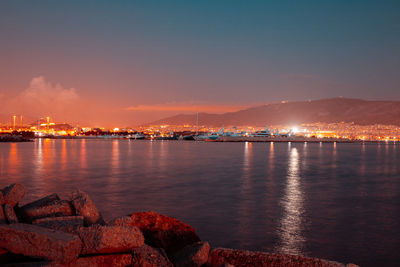 Illuminated city by sea against sky at night