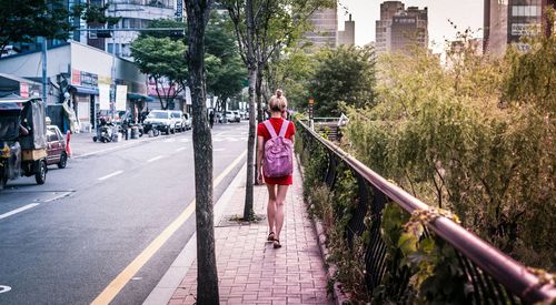 Rear view of girl walking on sidewalk by city street