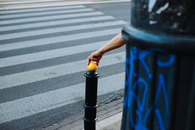 Cropped hand holding bollard by zebra crossing on street