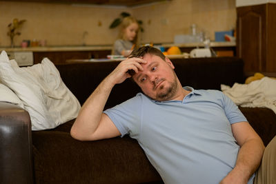 Tired single father resting on the couch against the background of his drawing daughter the father