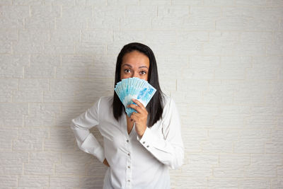 Portrait of young woman standing against white wall