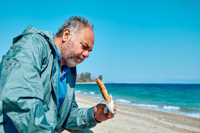 Bearded mature man at spring seaside eating hot palatable panzarotto 