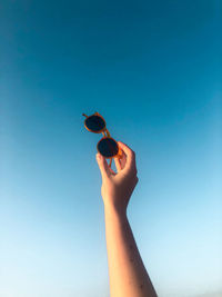 Low angle view of person hand against blue sky with sunglasses