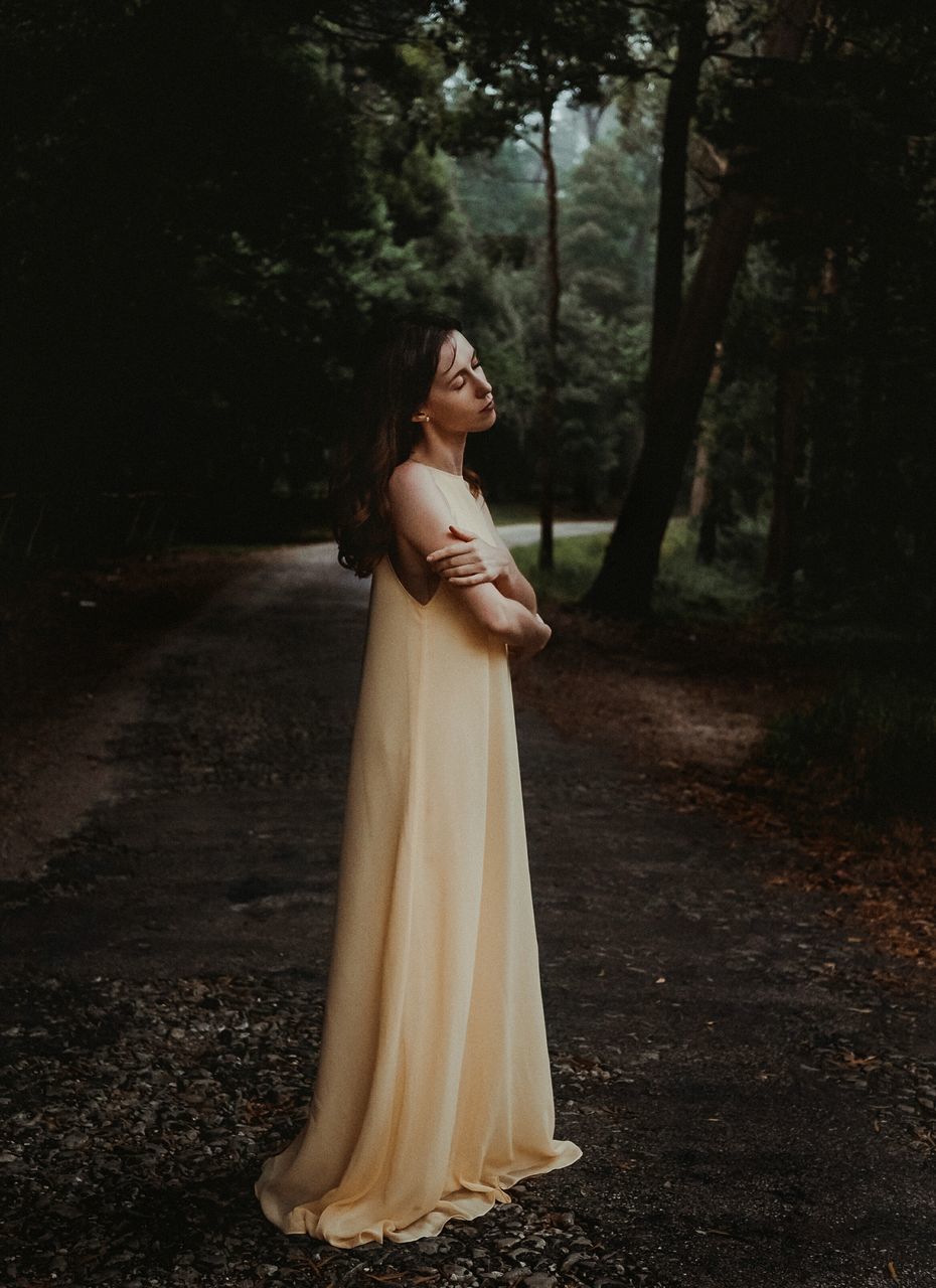 tree, young adult, standing, forest, land, women, plant, one person, young women, real people, lifestyles, adult, full length, side view, leisure activity, dress, nature, fashion, clothing, outdoors, beautiful woman, woodland, hairstyle, contemplation