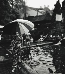 Woman standing under umbrella by pond during rainy season