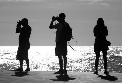 Silhouette people photographing on pier over sea during sunny day