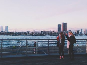 Rear view of people on river by cityscape against clear sky