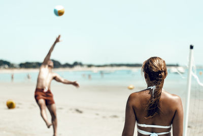 Rear view of woman looking at shirtless man playing beach volleyball